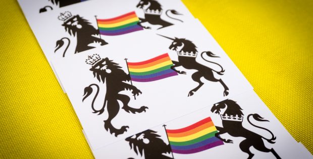 A photograph of pieces of card with a Government Crest on them, featuring the Pride rainbow flag