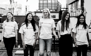 Black and white image of group of girls in front of cityscape. 